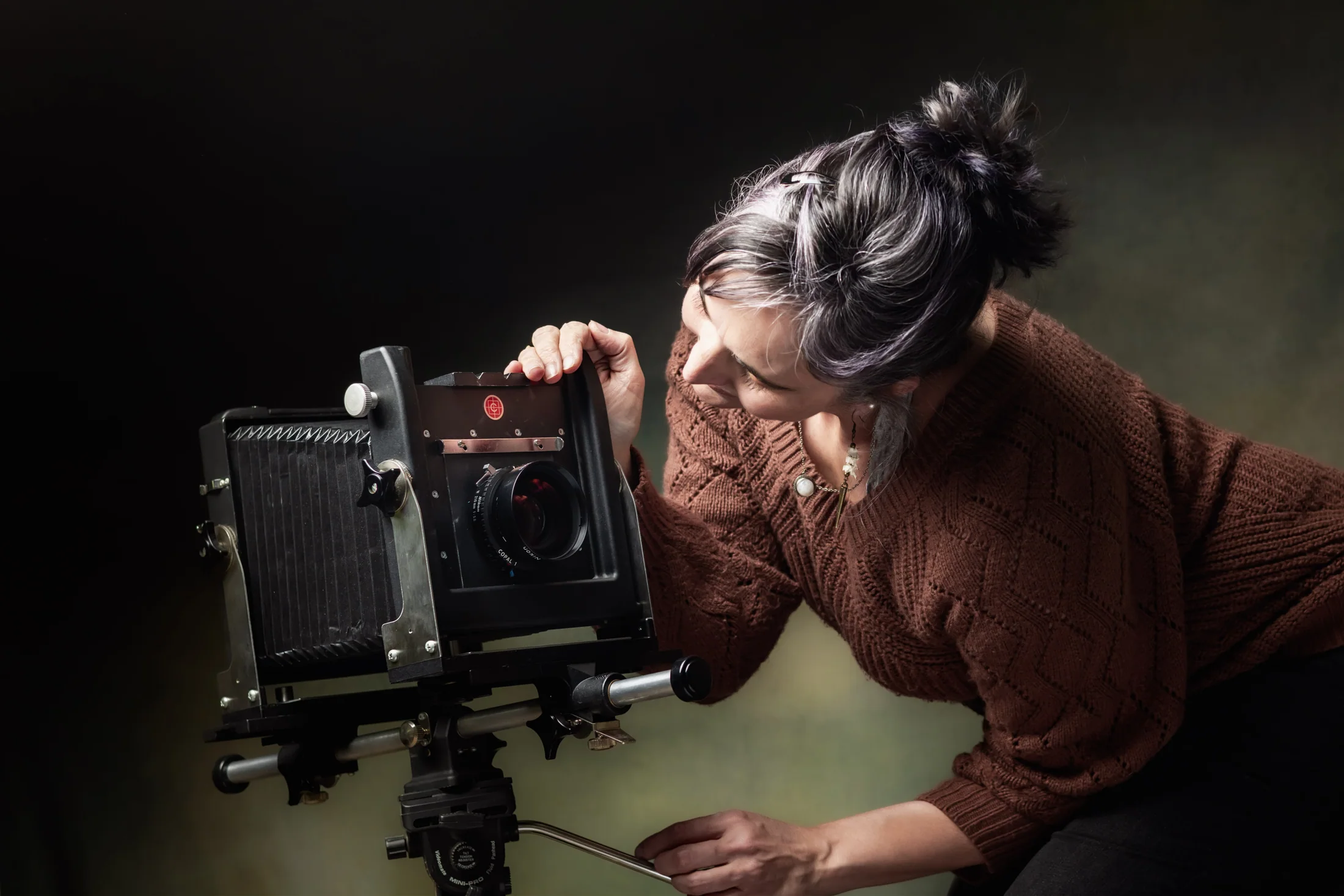 A photographer adjusts a large-format camera in a dark studio.